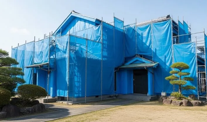 高圧洗浄中の住宅。建物全体が青いメッシュシート(養生)で隙間なく覆われ、近隣への汚水飛散を完全に防いでいる