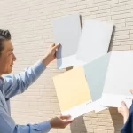 施主と業者がアパートの実際の外壁にA4サイズの塗り板を当てて色を確認している打ち合わせ風景