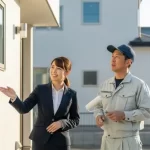 外壁塗装専門店の担当者と職人が、工事が完了した家の前で、施主であるお客様と満足そうに談笑している様子