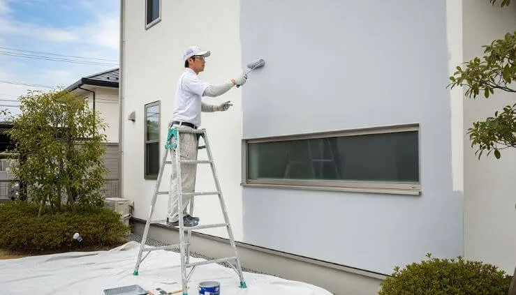 熟練の塗装職人が、住宅の外壁を丁寧にローラーで塗装している作業風景