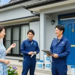 きれいに塗装された家の前で、施主である日本人女性と、作業着を着た塗装職人チームが和やかに談笑しており、工事の成功と顧客満足が感じられる