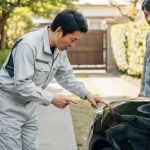車の塗料ミスト被害について、日本人塗装業者が車のオーナーに対し、真摯に状況を説明し謝罪しているリアルな写真。トラブルにも誠実に対応する会社の姿勢を示す。