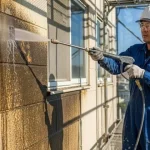 塗装職人が、塗装前の重要な下地処理として、高圧洗浄機で外壁の汚れを念入りに洗い流している
