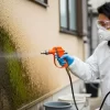 日本人の専門業者が、保護具を着用し、住宅の外壁に専用の噴霧器でバイオ洗浄剤を丁寧に塗布している様子