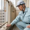 清潔な作業着を着た経験豊富な日本人職人が、マンションのバルコニーの劣化状況を真剣な表情で点検している