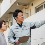 塗装専門店の担当者が、アパートのオーナー様に対して、外壁の劣化状況を指し示しながら建物診断の結果を丁寧に説明している場面