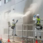 アパートの外壁を高圧洗浄機で丁寧に洗浄する日本の塗装職人。安全対策を徹底し、専門的な作業を行っている様子