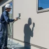 熟練の日本人塗装職人が、スプレーガンを使って塗料を住宅の外壁に丁寧に吹き付けている様子