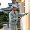 地域の塗装専門店の職人が、日本の住宅の外壁を丁寧にローラーで塗装している。専門性の高さと、施工品質へのこだわりを象徴する画像