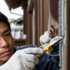 日本の住宅の外壁で、専門の職人が劣化した古いシーリングをカッターで丁寧に撤去している作業のクローズアップ