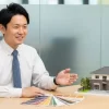 清潔感のある相談窓口で、外壁塗装のカラーサンプルや住宅模型を前に、専門家と相談している日本人顧客